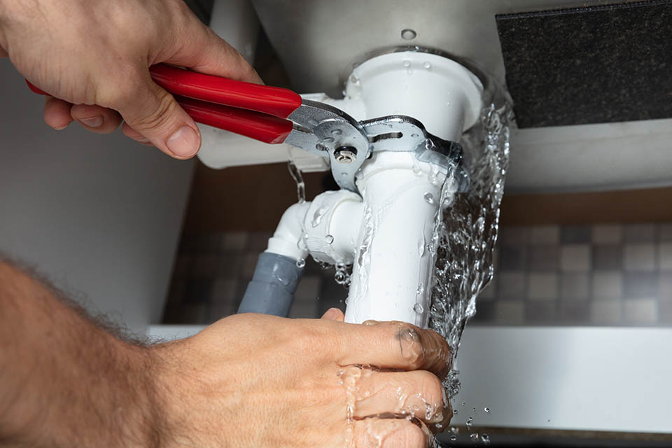Plumber Fixing Sink Pipe With Adjustable Wrench Plumber repairing a leaking pipe