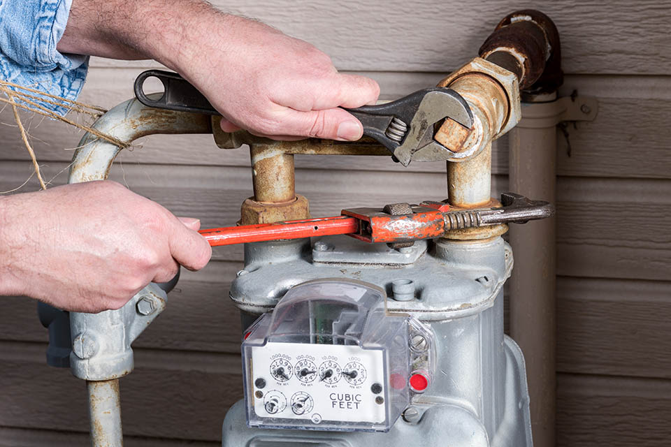 Technician working on an outdoor gas meter with tools Technician working on a home gas meter with tools